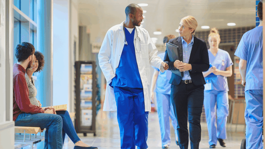A doctor and a lady in business attire walking through a hospital hallway.