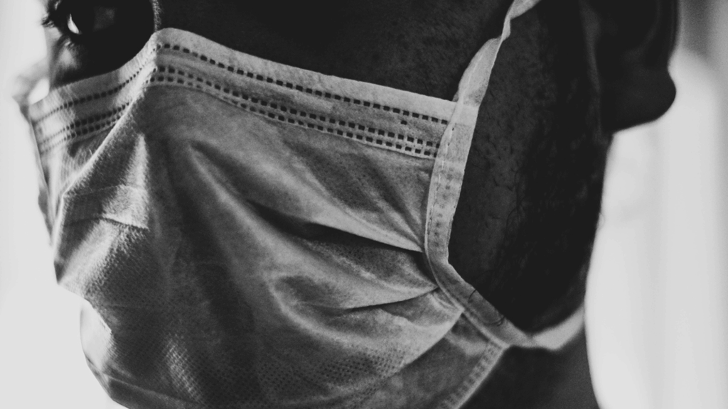 Black and white close-up image of a person wearing a surgical mask.