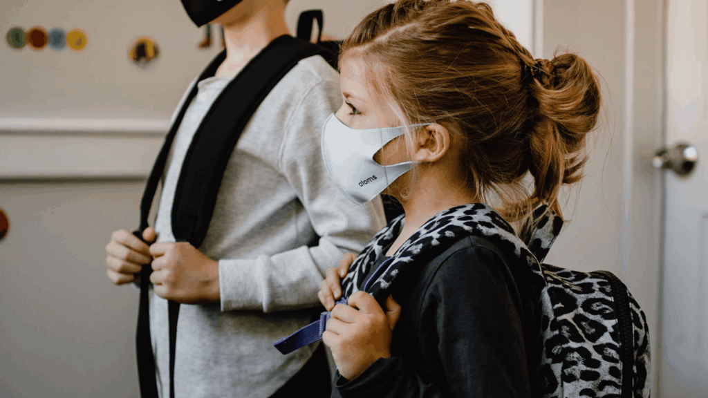 A young girl wears a mask and backpack in a school.