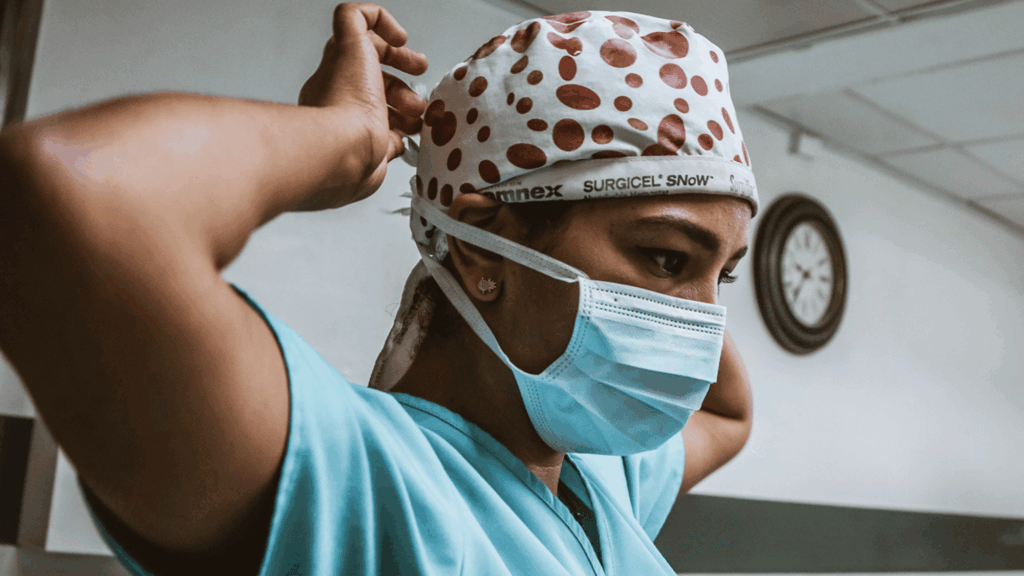 A masked healthcare worker putting on their haircap. 