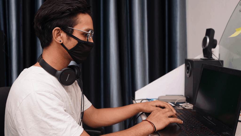 A person wearing a mask typing on their laptop.