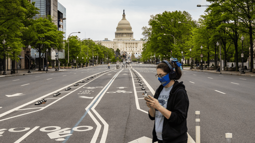 A person with a mask crossing the street in front of the United States Capitol.