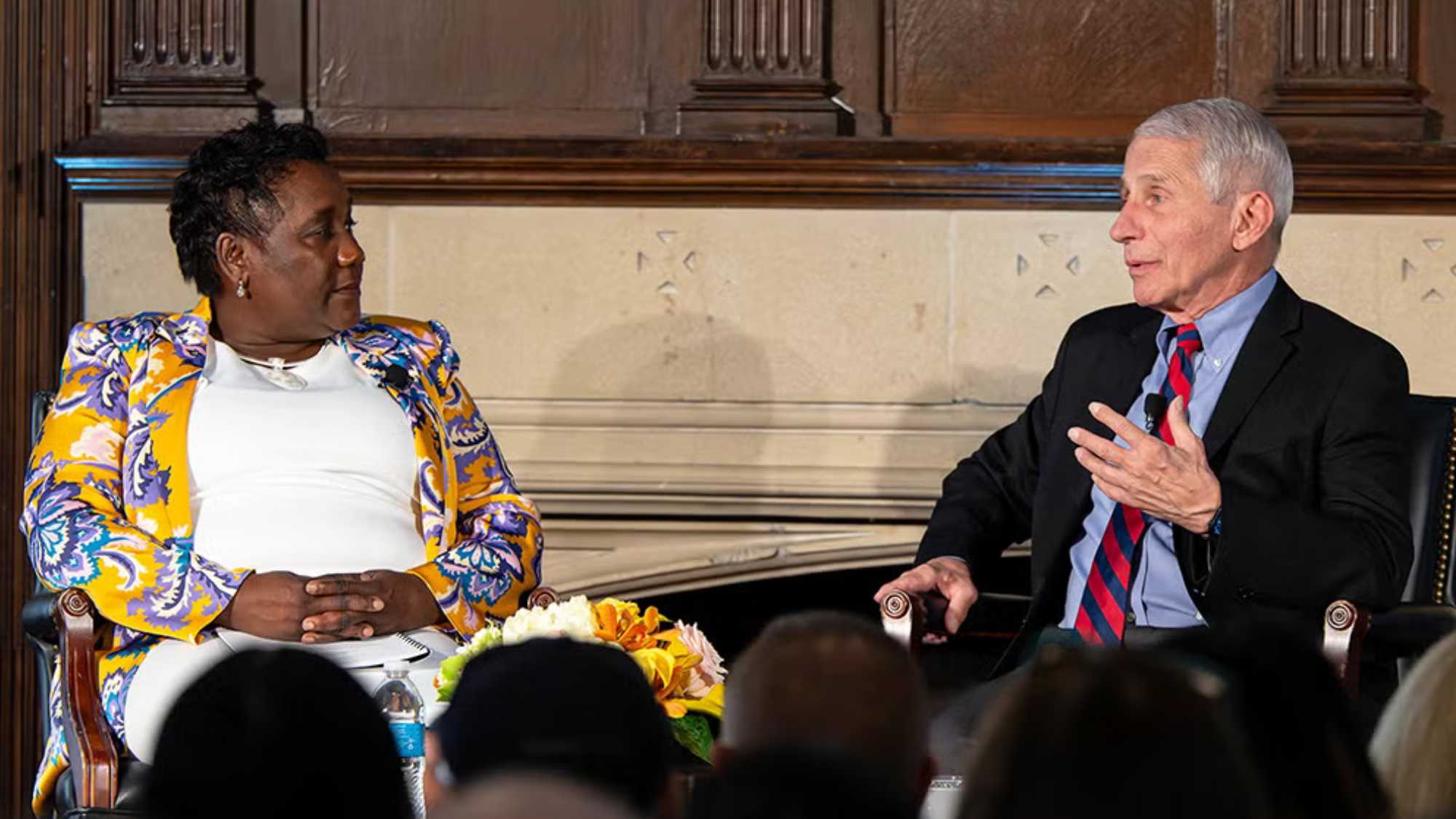 Roberta Waite and Anthony Fauci sit next to each other, talking in front of an audience.