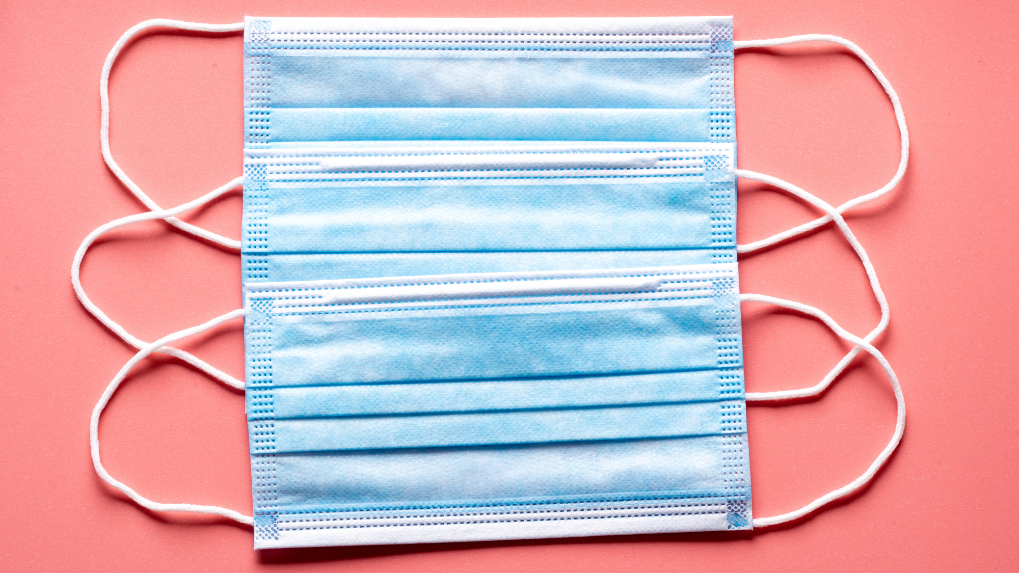 Two surgical masks against a pink background.